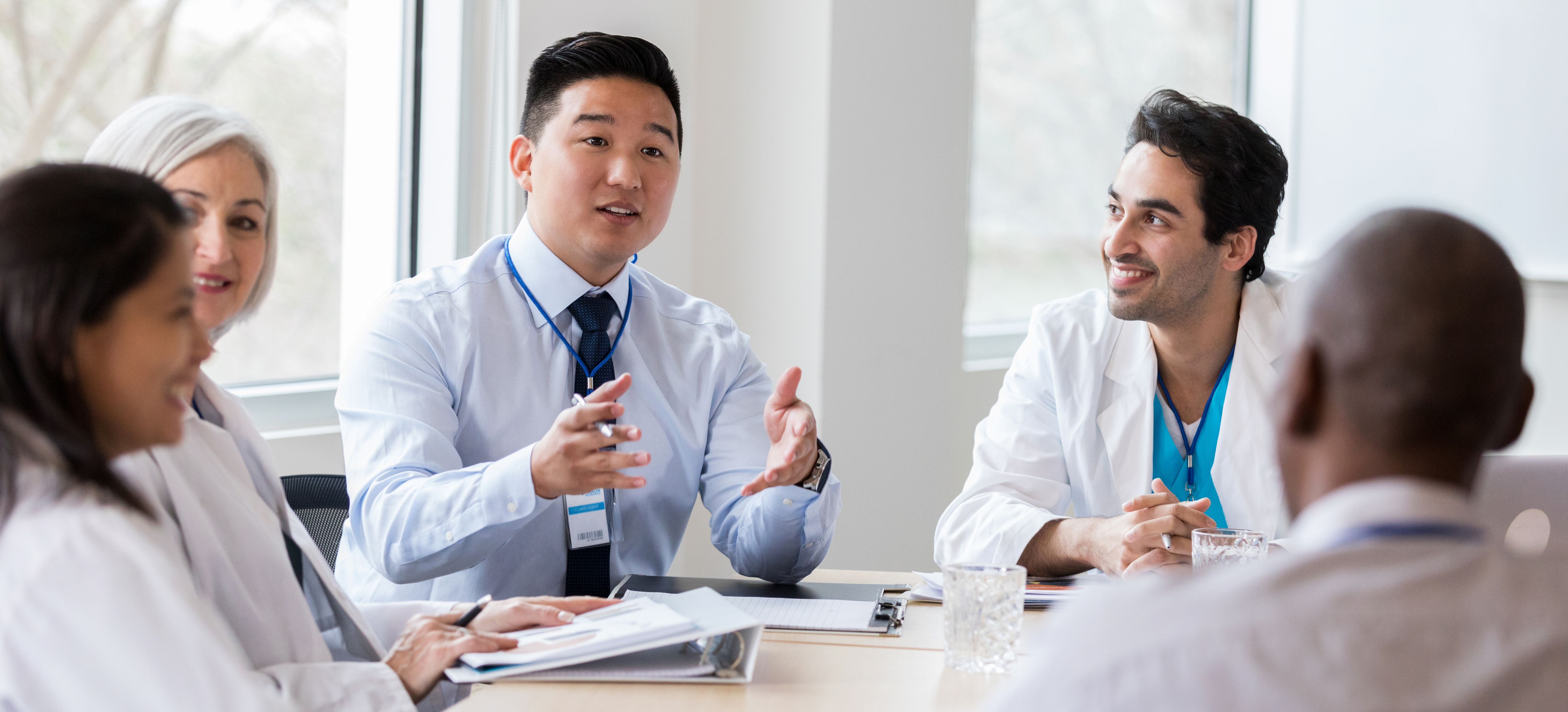 A professional man speaks to his 4 colleagueswhile sitting around a table.